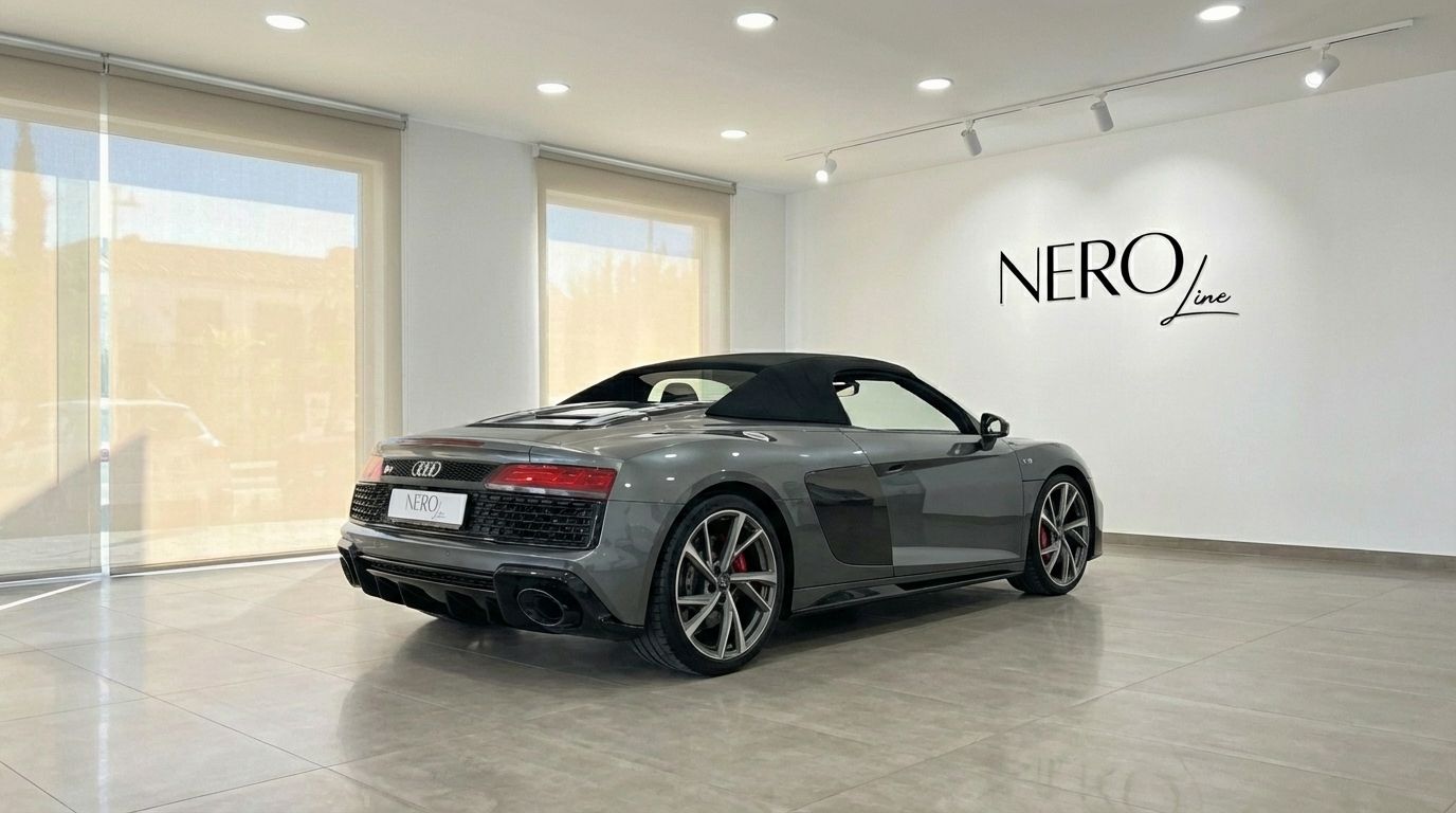 The metallic gray Audi R8 V10 Spyder Performance, with its black convertible top up, is parked in a showroom in Marbella.