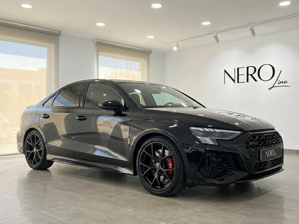Audi RS3 Saloon — Luxury Car Rental Marbella The sleek black Audi RS3 Saloon is showcased from a front three-quarter angle inside a bright showroom in Marbella.