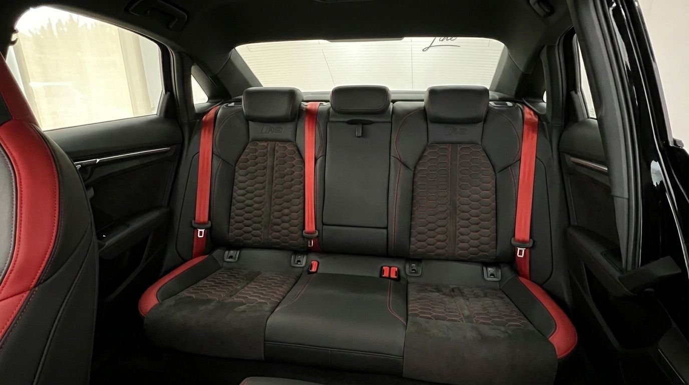 The luxurious rear interior of the Audi RS3 Saloon in Marbella, featuring black leather seats with red honeycomb stitching and striking red seatbelts.