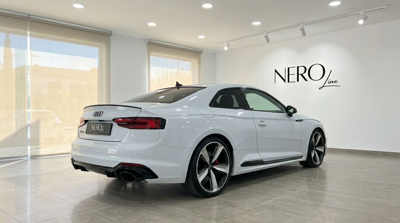The white 2021 Audi RS5 is showcased from a rear three-quarter angle in a bright showroom in Alicante.