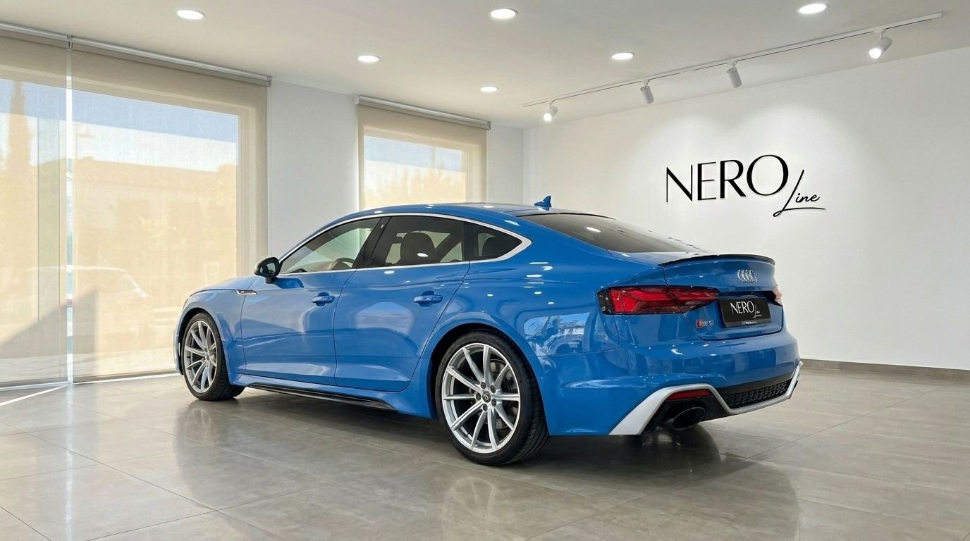 The blue 2020 Audi RS5 luxury car is showcased from a rear three-quarter view inside a modern showroom in Alicante.