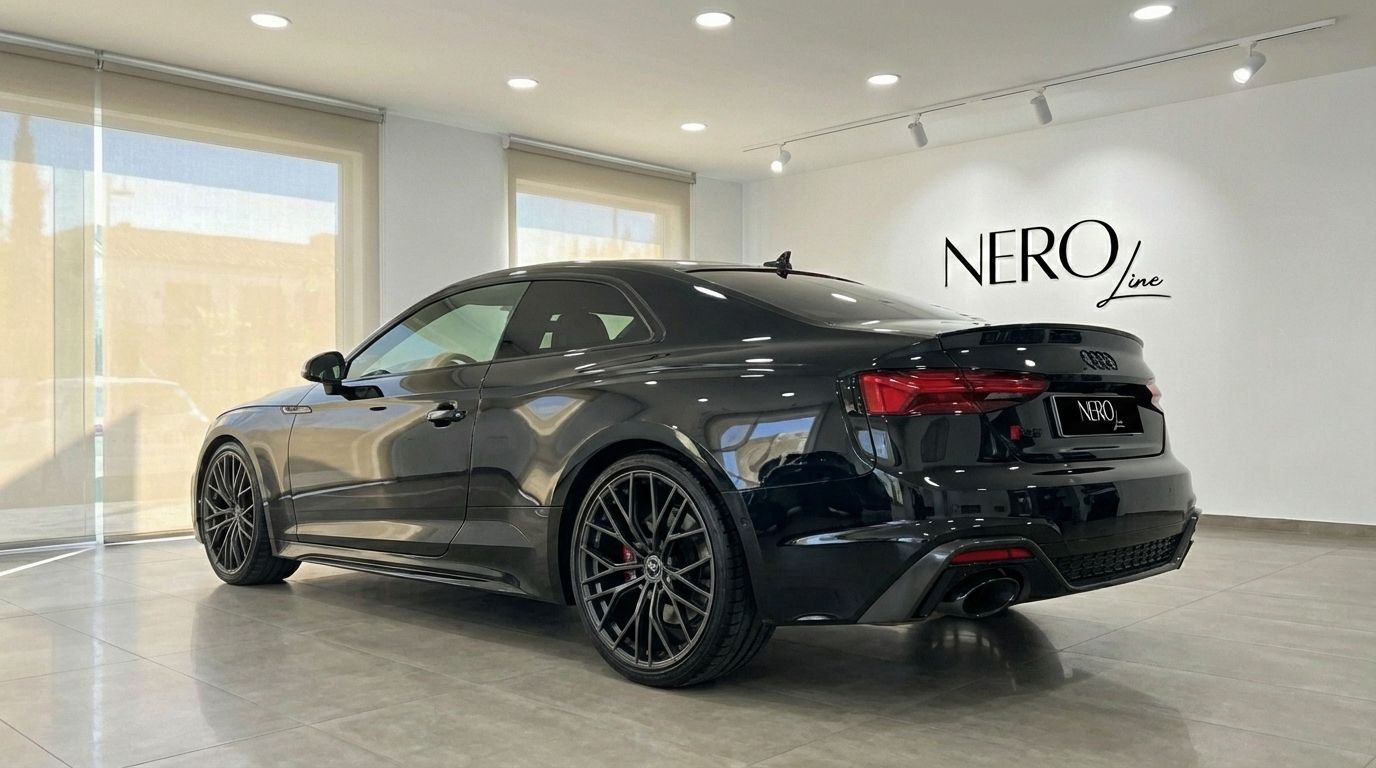 The black 2025 Audi RS5 luxury sedan is showcased from a rear three-quarter view, parked indoors in Marbella.