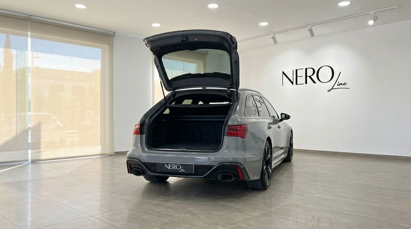 The gloss Nardo Grey Audi RS6 Avant is seen from the rear with its spacious trunk open, parked in a bright showroom in Ibiza.
