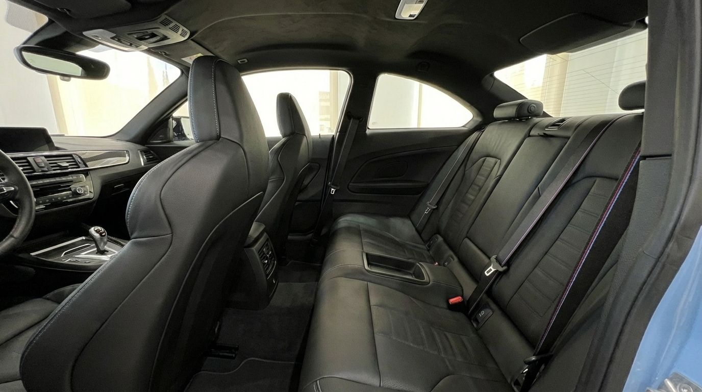 The luxurious black leather interior of the BMW M2 Competition, showcasing the rear seats and a glimpse of the front cabin in Alicante.