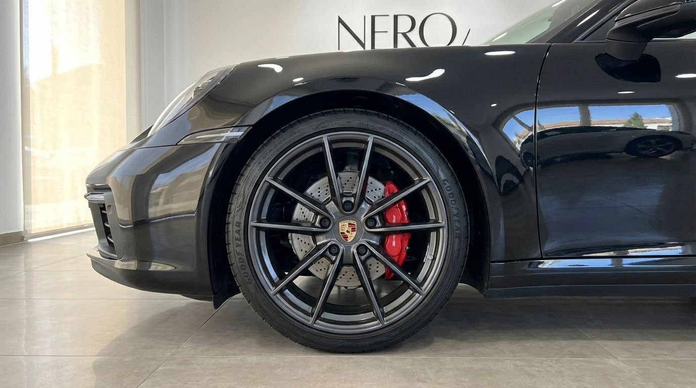Primer plano de la rueda delantera izquierda del Porsche 911 Carrera S Cabrio negro, con llantas multirradio grises y pinzas de freno rojas en Madrid.