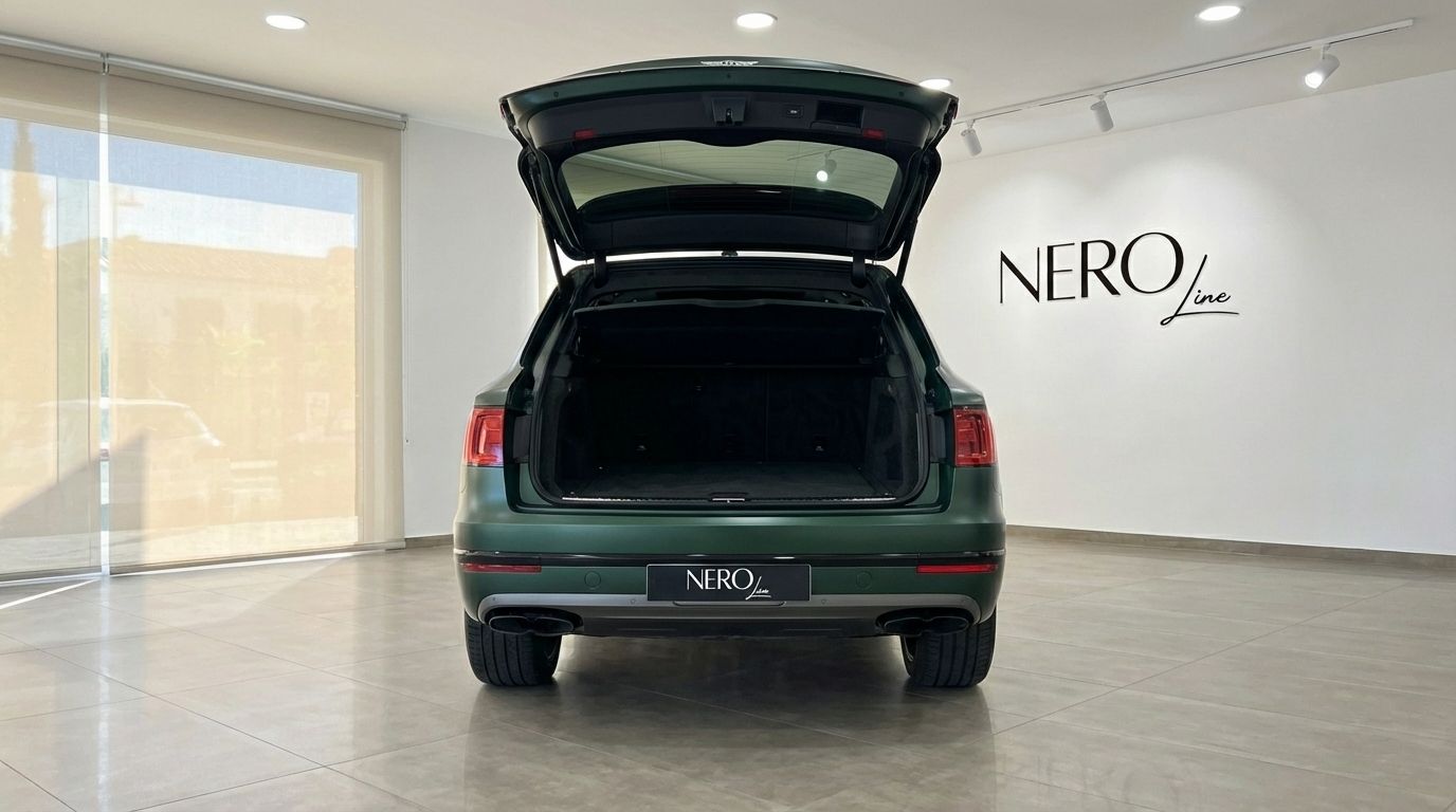 The rear view of a 2019 Bentley Bentayga in Satin British Racing Green with its trunk open, displayed in a showroom in Valencia.