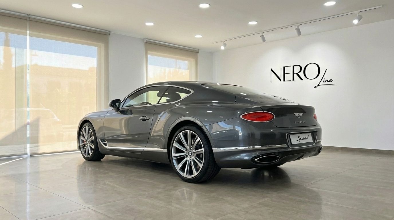 The gunmetal gray Bentley Continental GT Speed V12 is showcased from a rear three-quarter view in a bright Alicante showroom.
