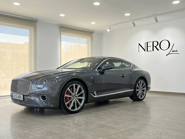 Bentley Continental GT Speed V12 — Alicante Showroom The gunmetal gray Bentley Continental GT Speed V12 is showcased from the front three-quarter view in a showroom in Alicante.