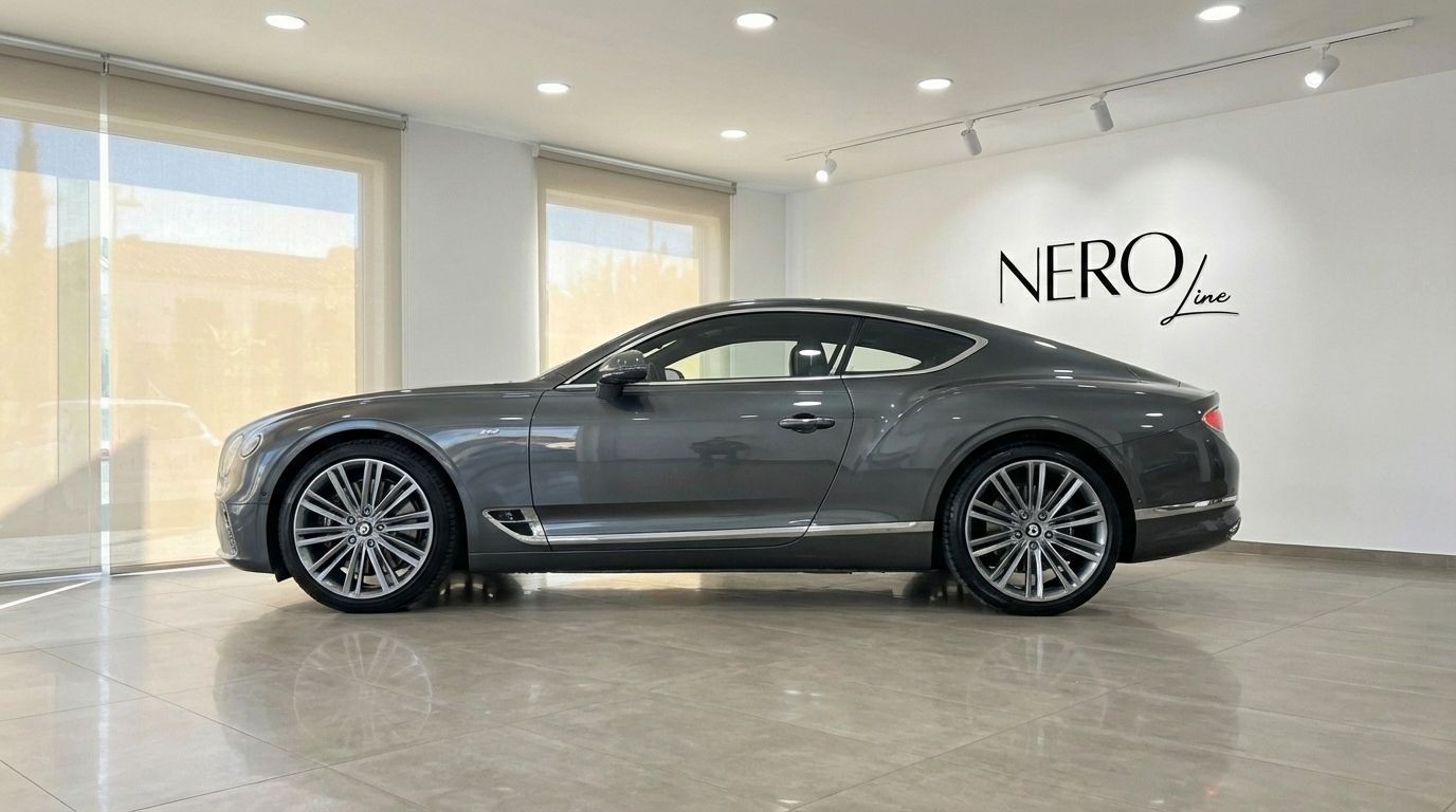 The gunmetal gray 2021 Bentley Continental GT Speed V12 is showcased in a modern Alicante showroom, viewed from its elegant side profile.