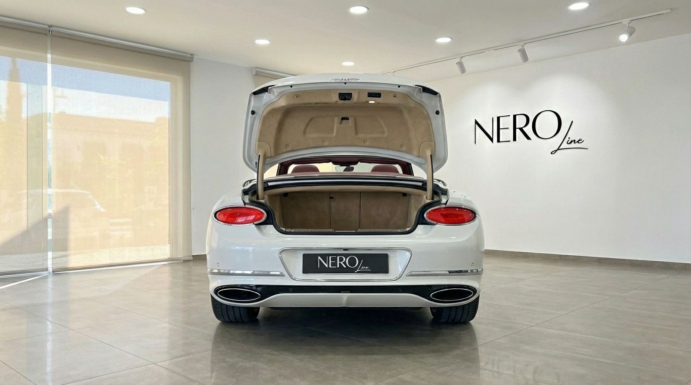 The rear view of a pearl white Bentley Continental GTC with its trunk open, parked in a showroom in Barcelona.