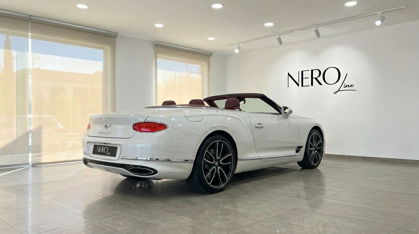The pearl white Bentley Continental GTC convertible, with its red interior and top down, is showcased from a rear three-quarter view in a Barcelona showroom.