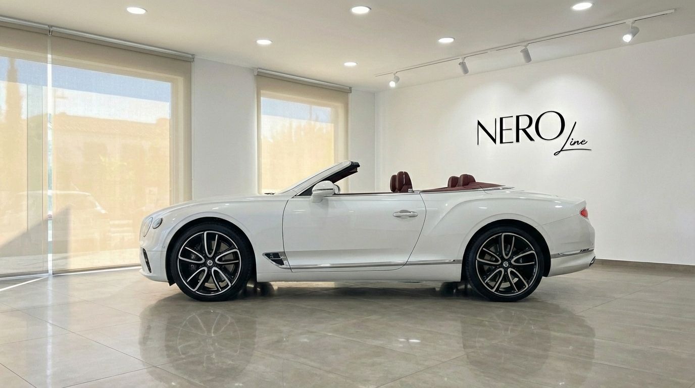 A white Bentley Continental GTC convertible with a red interior, viewed from the side in a modern showroom.