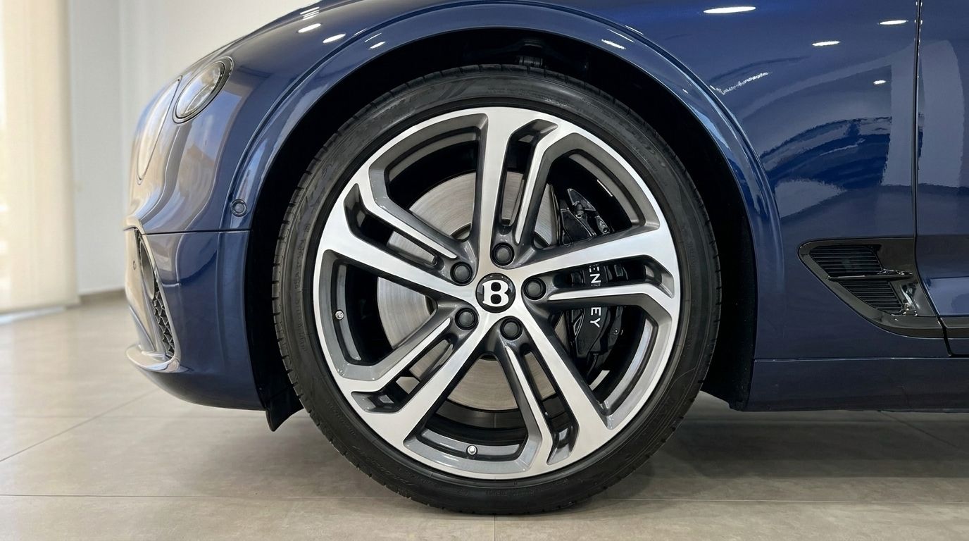 The Bentley Continental GTC's front wheel with multi-spoke alloy rim and dark sapphire blue bodywork is visible in Barcelona.