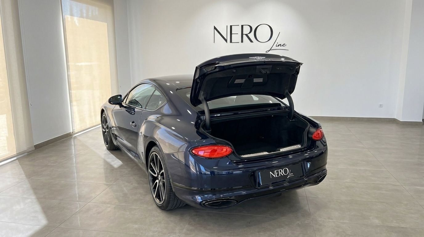 The dark blue Bentley Continental GTC Speed W12 is shown from the rear with its trunk open, inside a bright showroom in Barcelona.