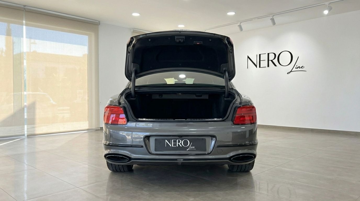 The metallic gray Bentley Flying Spur Special is shown from the rear with its trunk open, parked in a Marbella showroom.