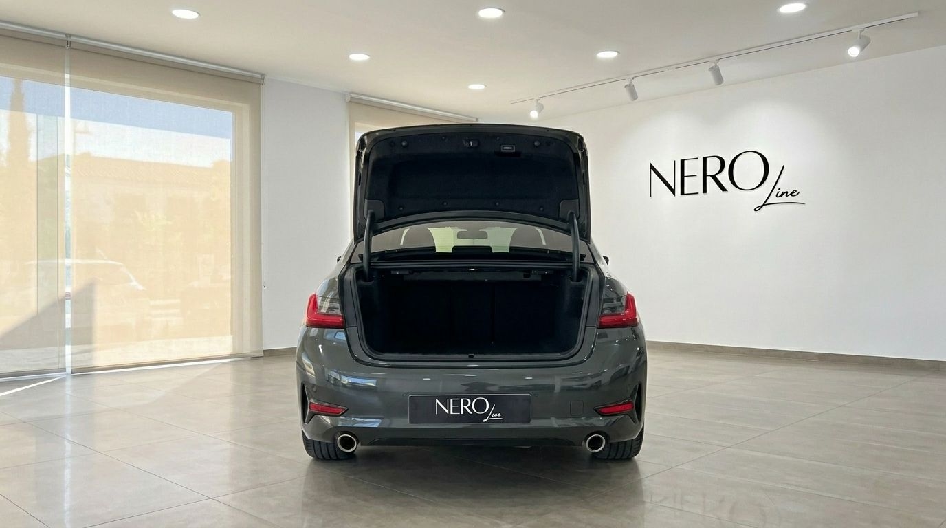 The rear view of a dark grey BMW 320d with its trunk open, showcasing ample storage space in a bright showroom in Alicante.