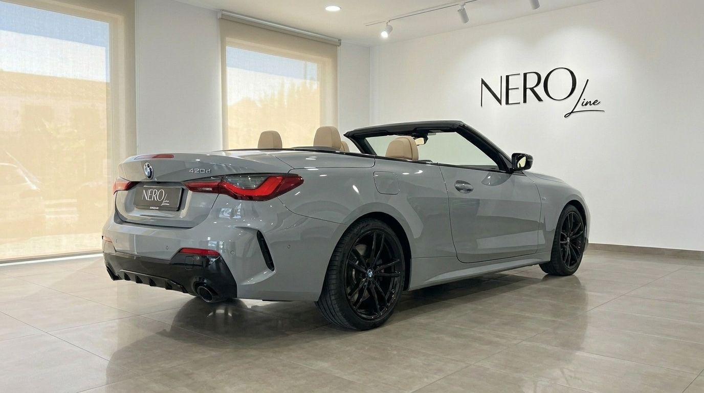 The metallic Brooklyn Grey BMW 420d Cabriolet, with its top down and beige interior, is showcased from a rear three-quarter angle in a Marbella showroom.