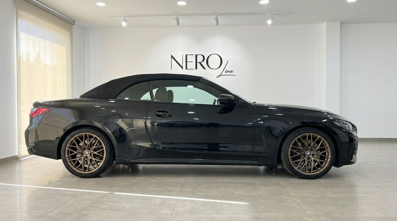 The black 2023 BMW 430i M Convertible with its soft top up is parked indoors in Benidorm, showcasing its side profile.
