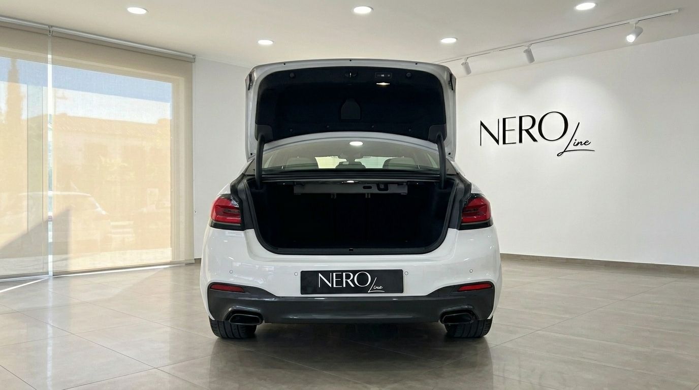 The white BMW 530e xDrive is shown from the rear with its trunk open, highlighting its spacious storage in a showroom in Alicante.