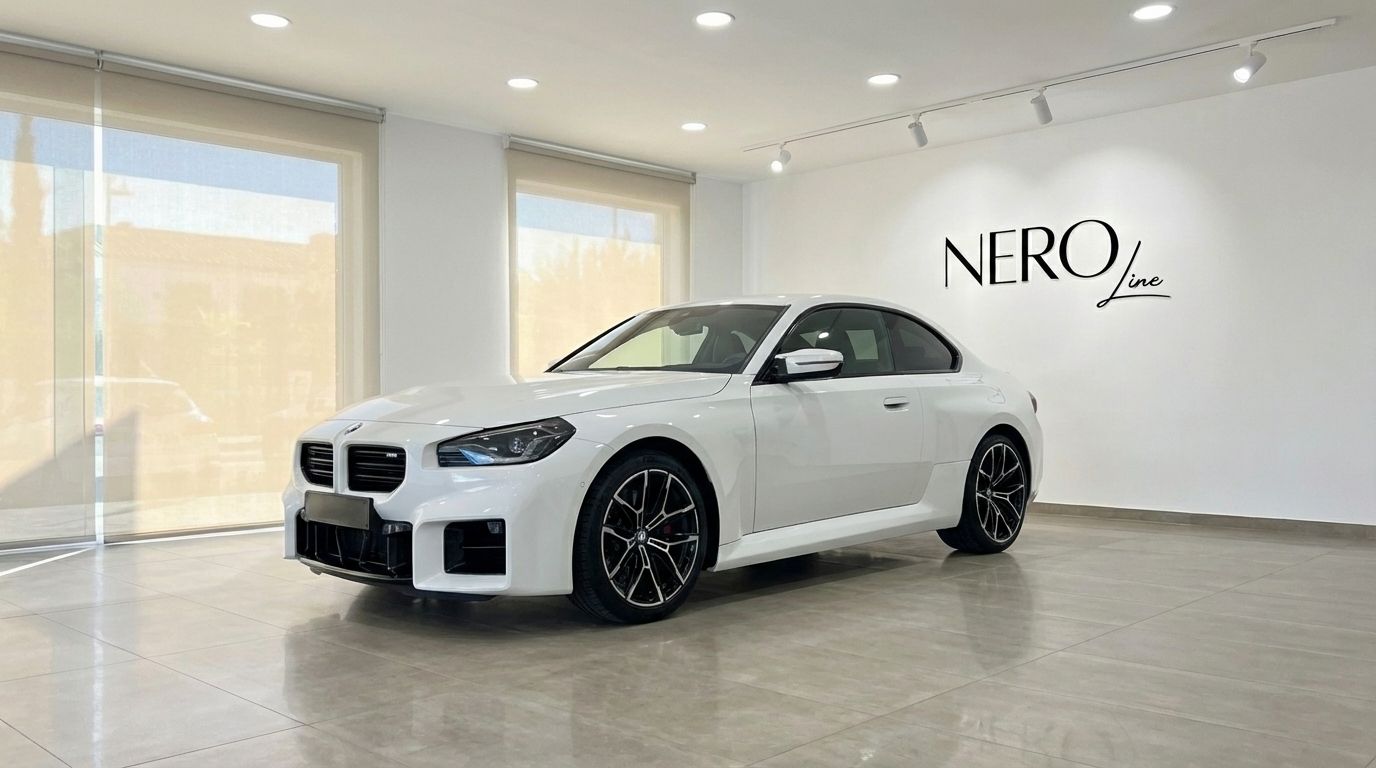 El BMW M2 Competition blanco de 2025 se exhibe desde un ángulo frontal tres cuartos en un moderno showroom de Nero Line en Madrid.
