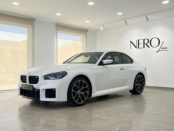 BMW M2 Competition — Alquiler de coches de lujo Madrid El BMW M2 Competition blanco de 2025 se exhibe desde un ángulo frontal tres cuartos en un moderno showroom de Nero Line en Madrid.