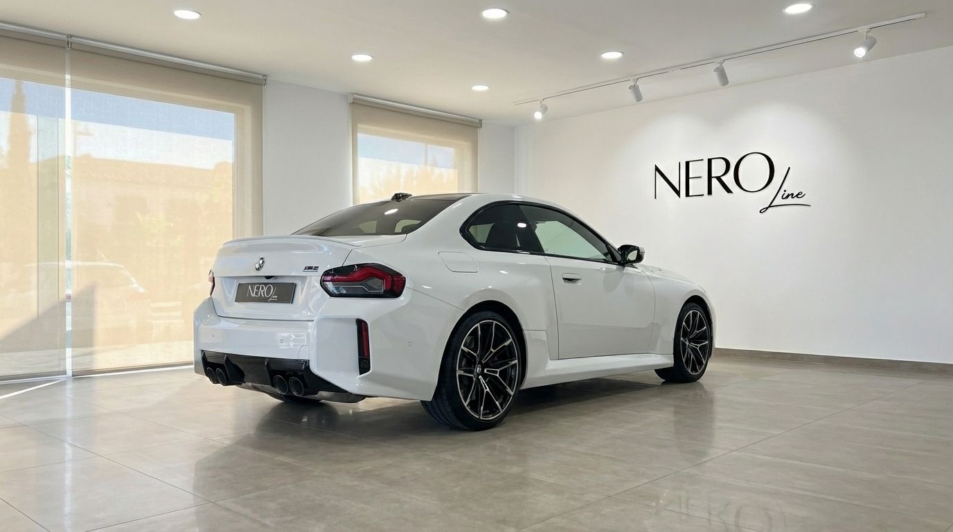 El BMW M2 Competition blanco de 2025 se exhibe desde un ángulo trasero de tres cuartos en una luminosa sala de exposiciones en Madrid.