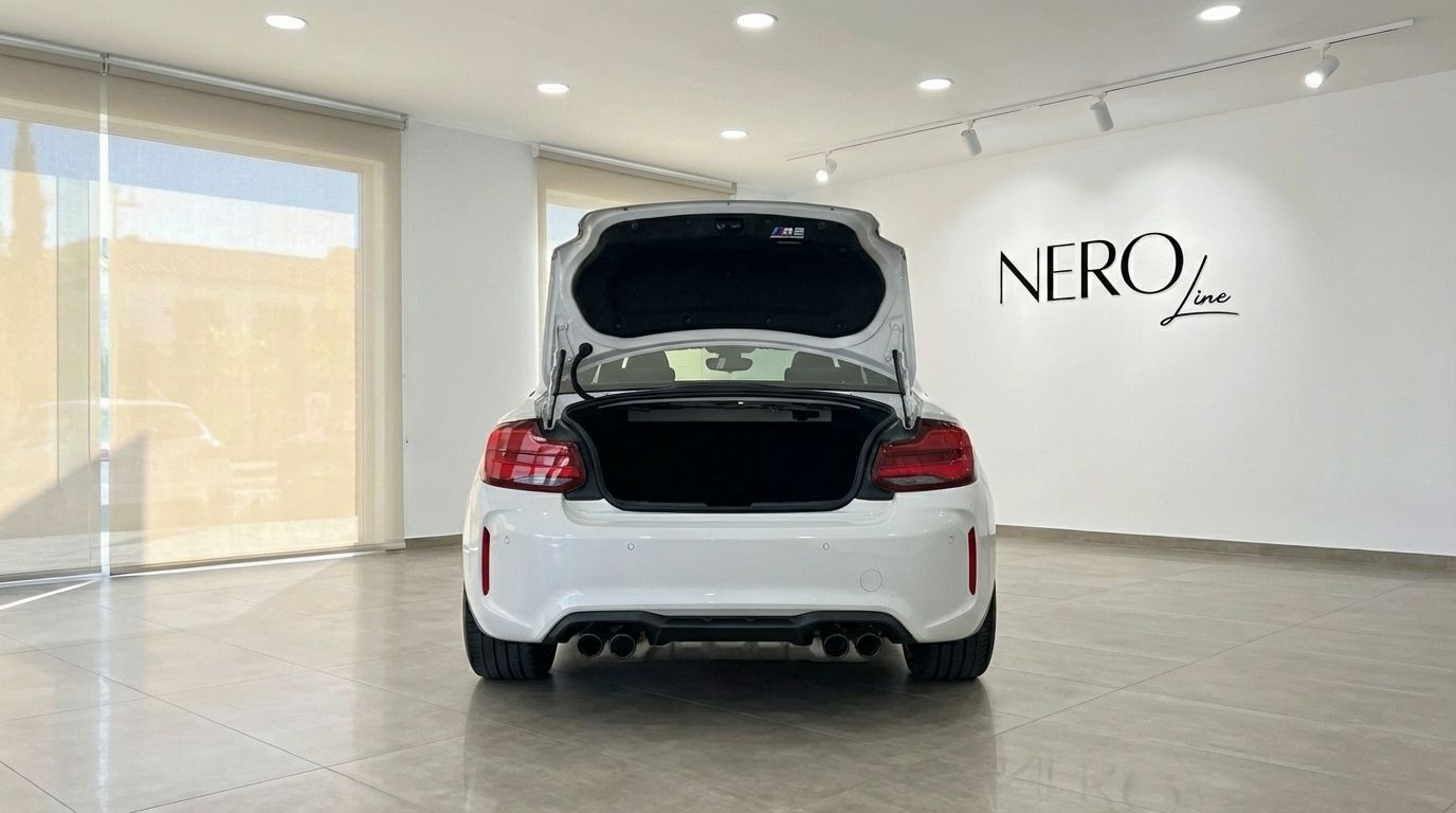 El BMW M2 Competition blanco de 2025 se muestra desde la parte trasera con el maletero abierto, aparcado en un concesionario en Madrid.