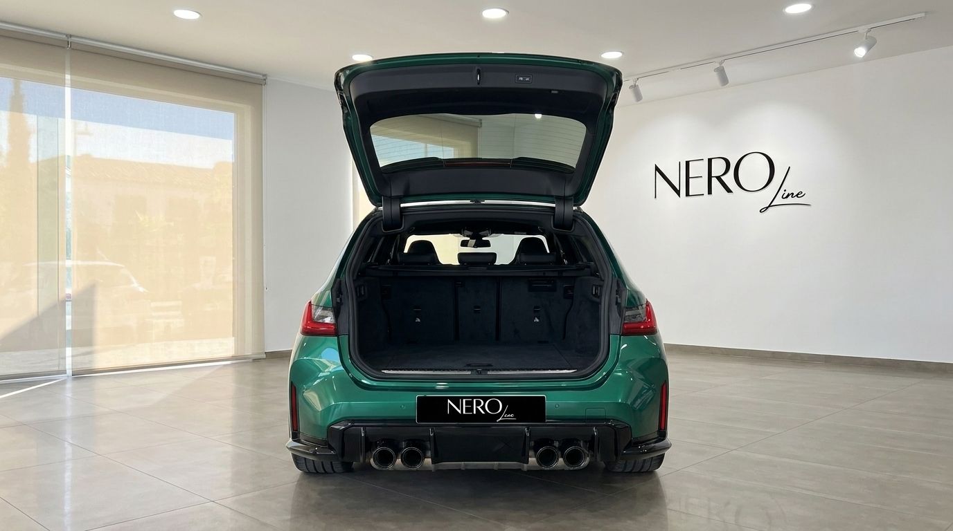 The rear view of the metallic Isle of Man Green BMW M3 Touring Competition xDrive with its trunk open, parked in a showroom in Marbella.
