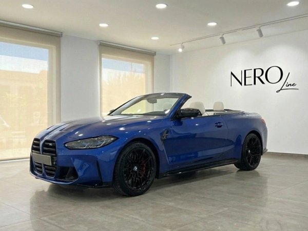 BMW M4 Competition Convertible — Showroom in Barcelona The metallic blue 2025 BMW M4 Competition Convertible, with its top down and white interior, is showcased in a Barcelona showroom.