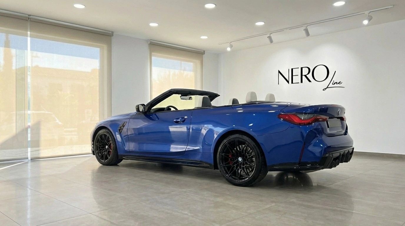 The metallic blue BMW M4 Competition Convertible is showcased from a rear three-quarter angle with the top down in a Barcelona showroom.