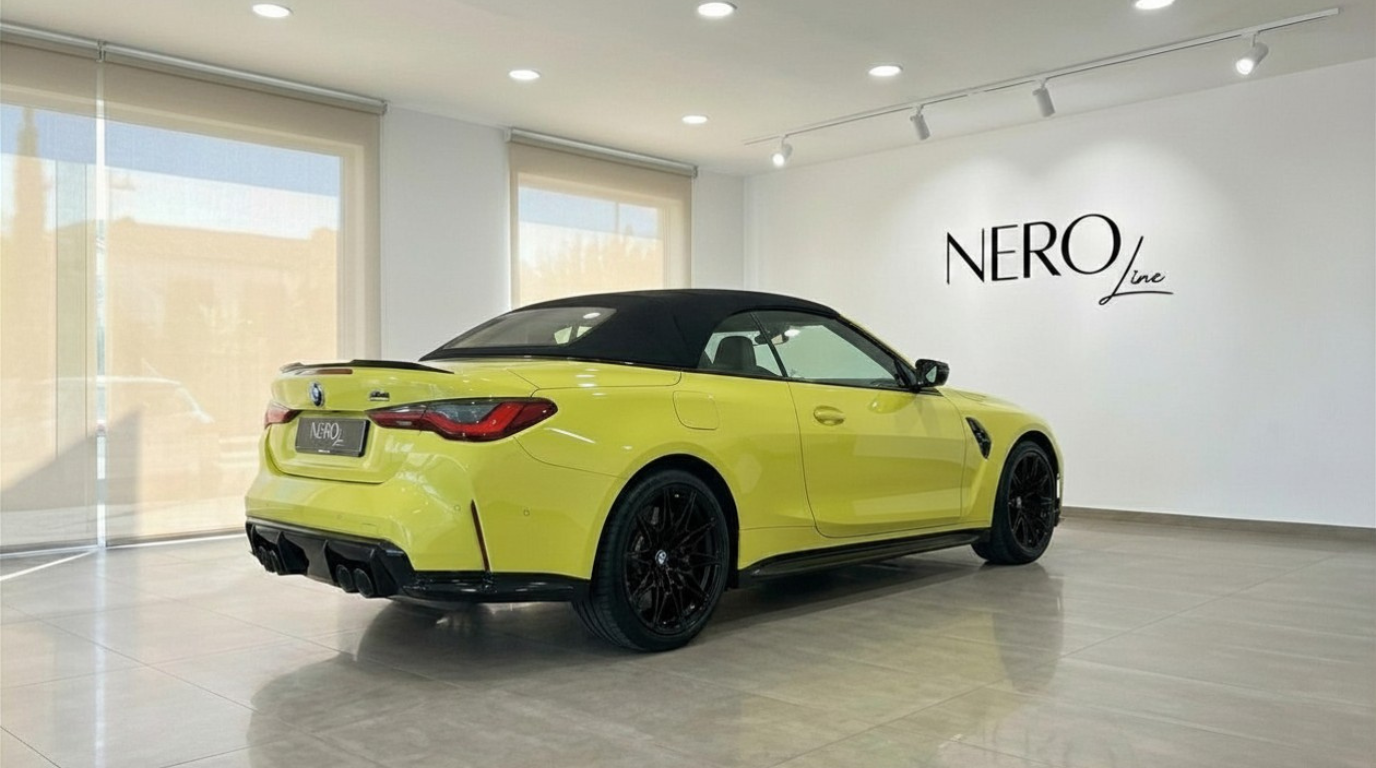 La BMW M4 Competition Convertible xDrive jaune Sao Paulo brillant, avec sa capote noire, est vue de trois quarts arrière dans un showroom à Marbella.