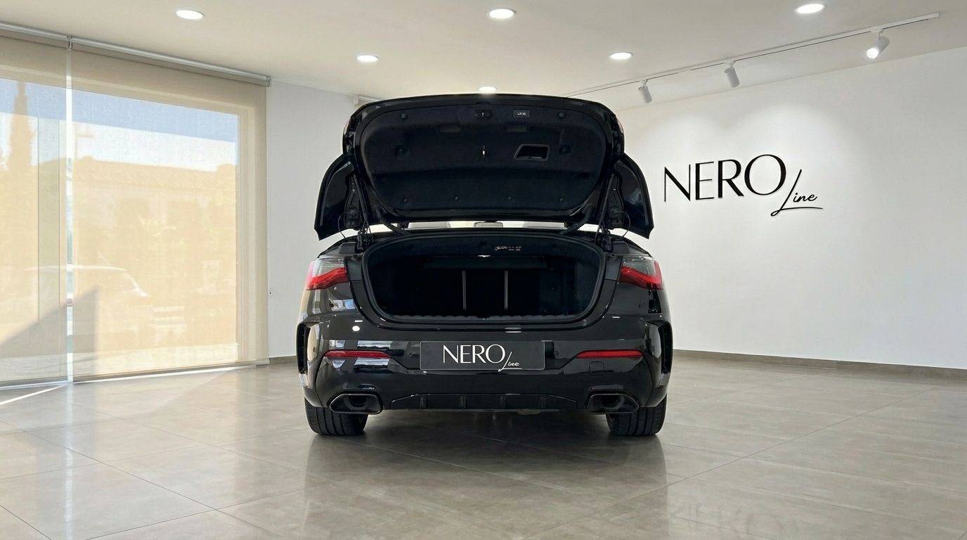 Vista trasera de un BMW M440i Cabrio 2023 negro brillante con el maletero abierto, aparcado en un concesionario en Madrid.