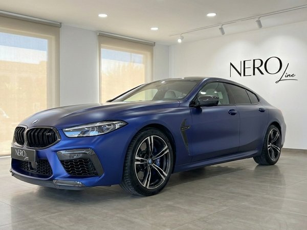BMW M8 Competition Gran Coupe — Showroom Marbella The matte blue BMW M8 Competition Gran Coupe is showcased from a front three-quarter view inside a modern showroom in Marbella.