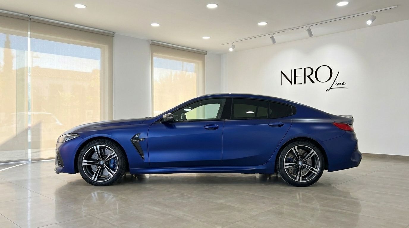 The matte blue BMW M8 Competition Gran Coupe is showcased from its sleek side profile in a luxury showroom in Marbella.