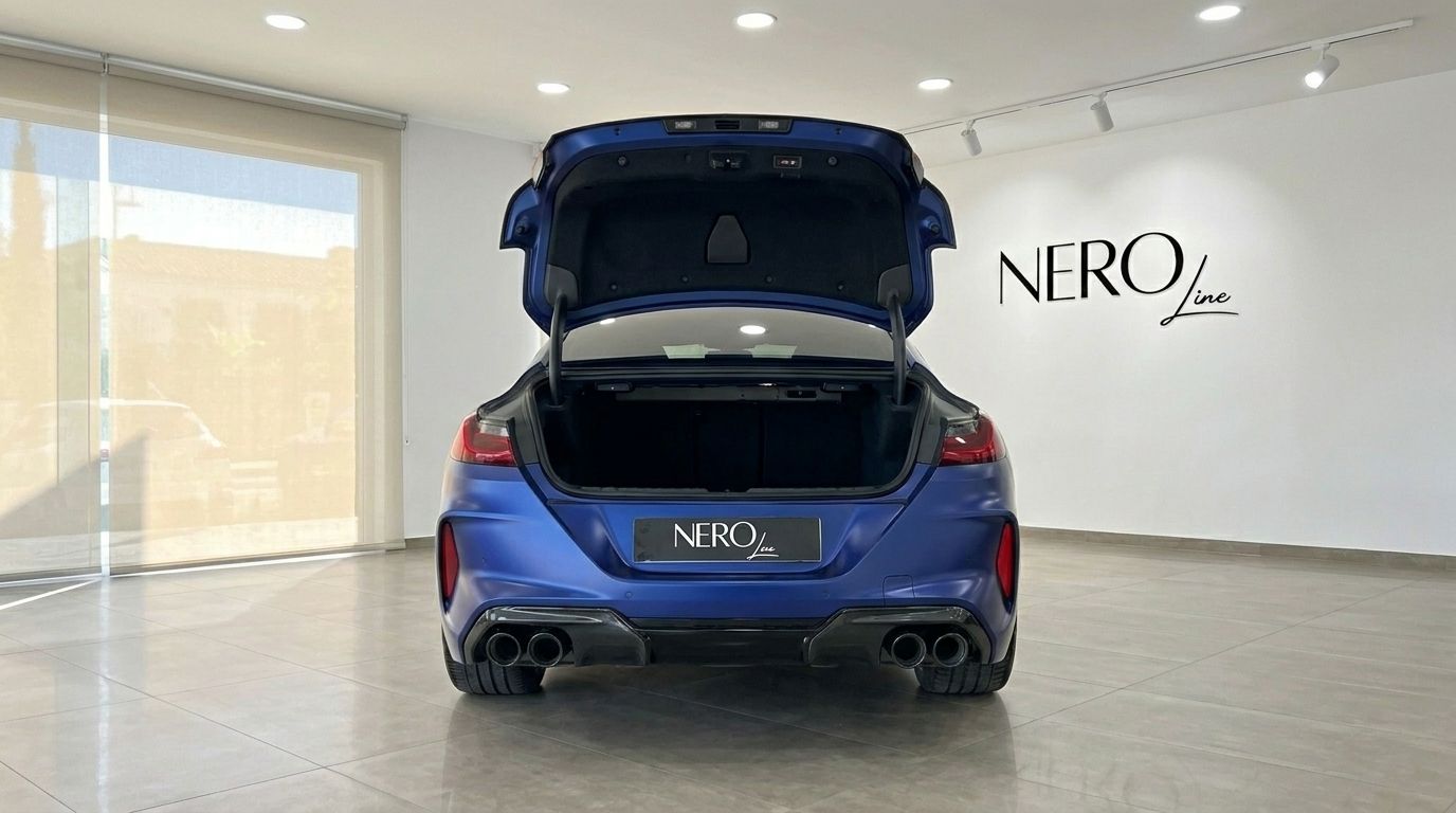 The rear view of the matte blue BMW M8 Competition Gran Coupe with its trunk open, displayed in a showroom in Marbella.