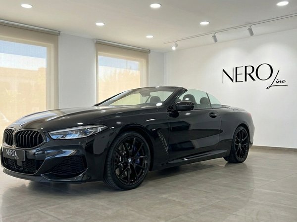 BMW M850 Convertible — Showroom in Alicante The sleek gloss black 2021 BMW M850 convertible is showcased with its top down in a bright showroom in Alicante, offering a luxurious front three-quarter view.