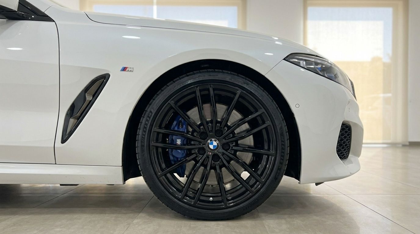 The white BMW M850i Cabriolet's front wheel with black multi-spoke rim and blue brake caliper is visible in Alicante.