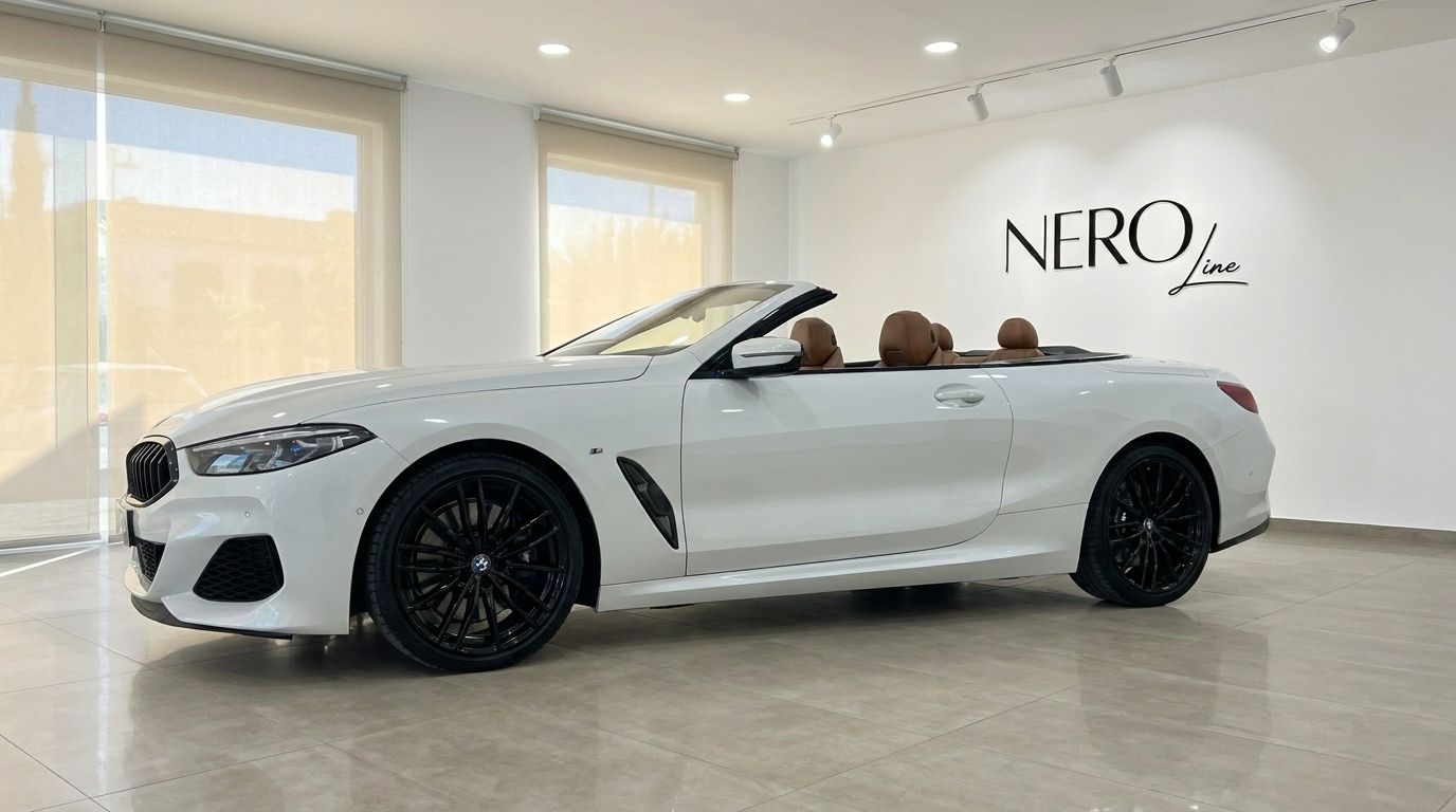 The white BMW M850i Cabriolet is showcased from the side with its top down, revealing the luxurious brown interior in Alicante.