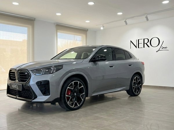 BMW X2 M35i xDrive — Front three-quarter view The 2024 BMW X2 M35i xDrive in gloss metallic grey is showcased from a front three-quarter angle in a Marbella showroom.