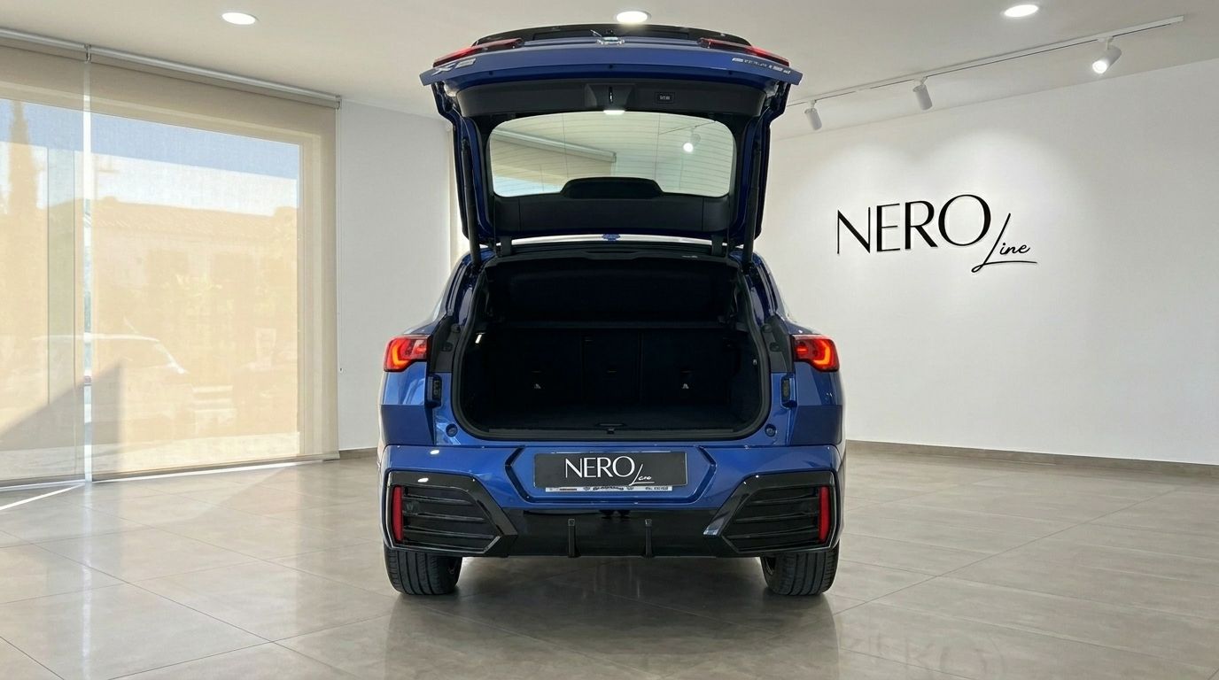 The blue 2025 BMW X2 is shown from the rear with its trunk open, highlighting the spacious cargo area in a showroom in Alicante.