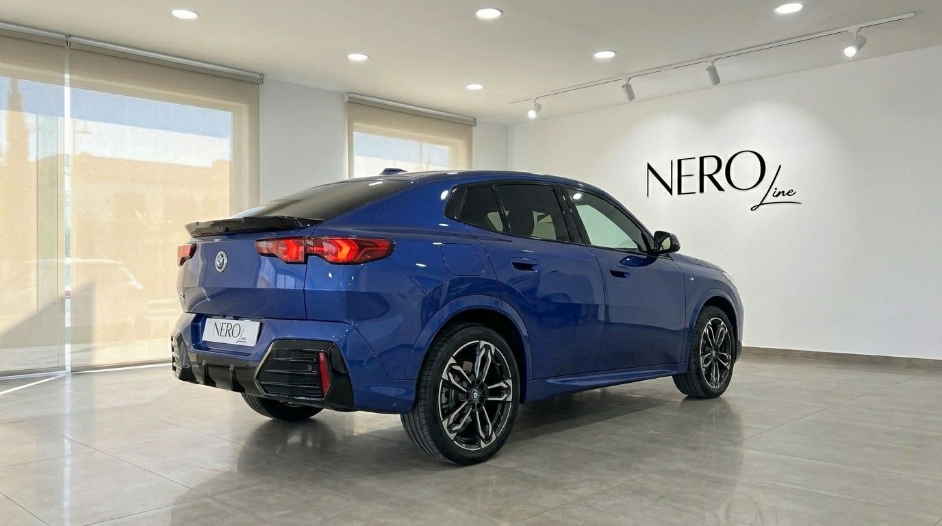 A striking blue 2025 BMW X2 is showcased from its rear three-quarter angle in a modern showroom in Alicante.