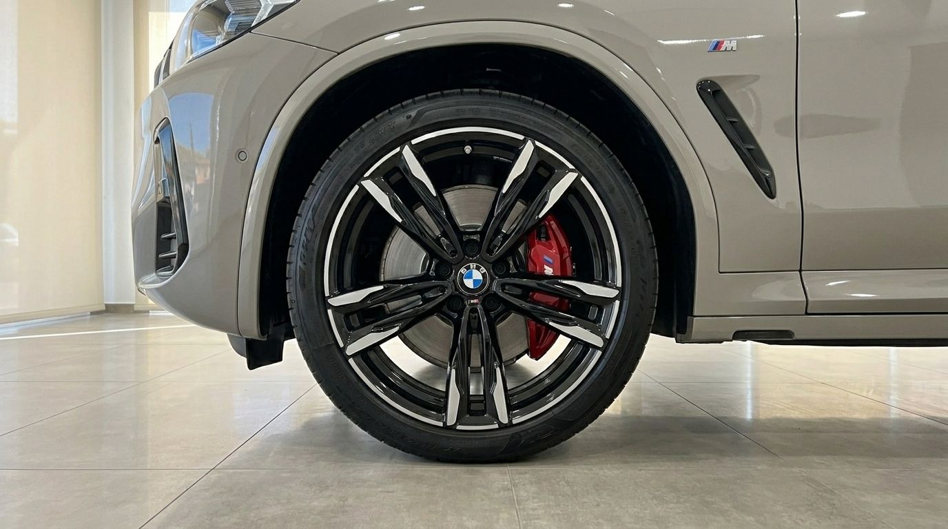 The front wheel of the BMW X3 M50i xDrive in Gloss Dune Grey, showcasing its black and silver rim with red brake caliper in Marbella.