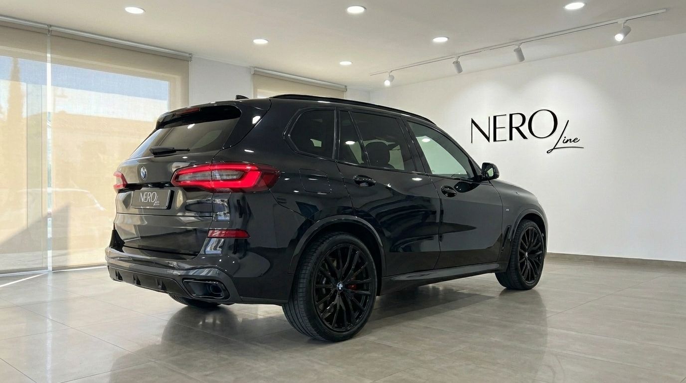 Un SUV BMW X5 xDrive M Sport noir brillant est présenté de trois quarts arrière dans un showroom à Marbella.