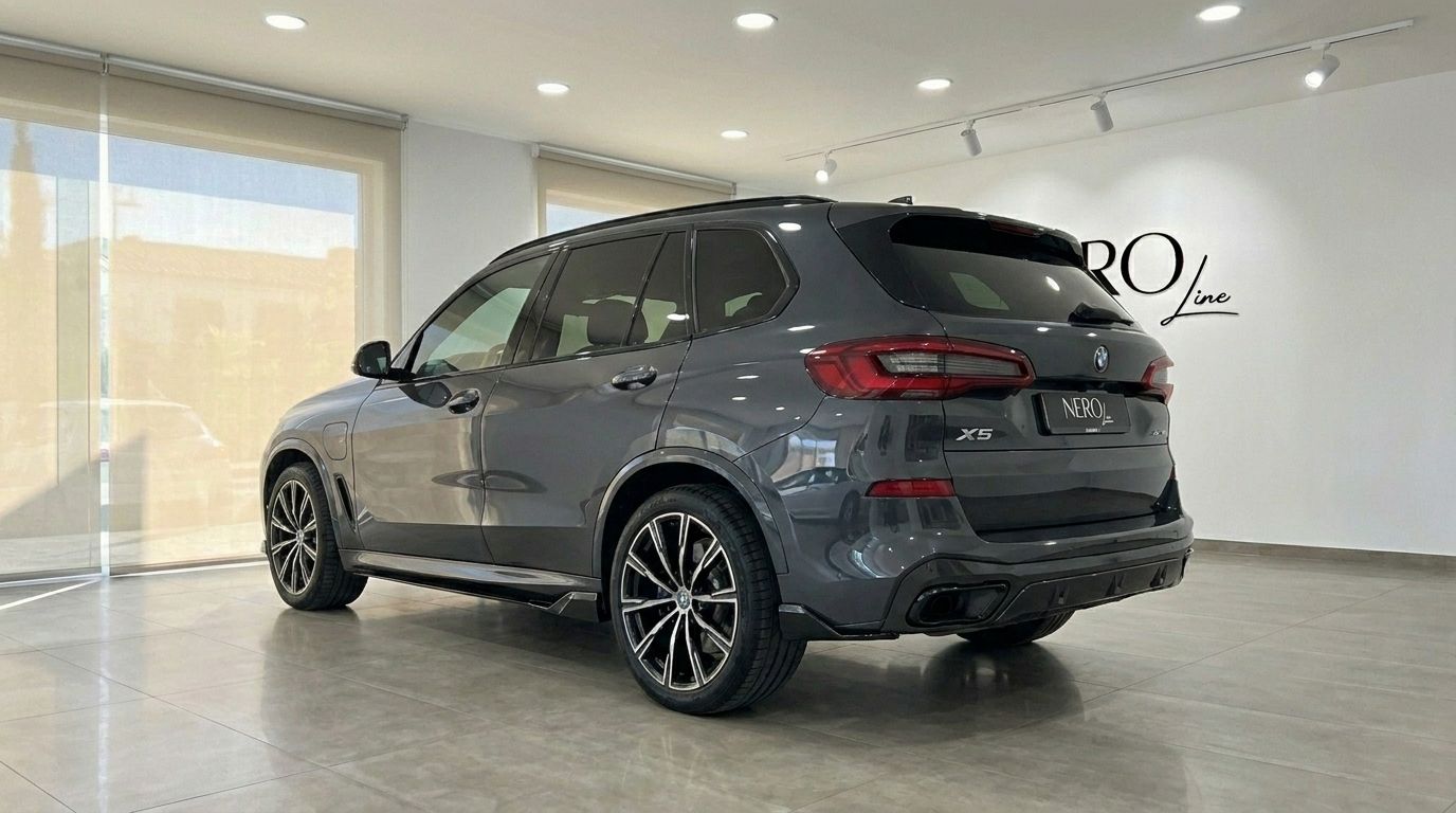 The dark grey 2021 BMW X5 xDrive45e is shown from its rear three-quarter angle inside a showroom in Alicante.