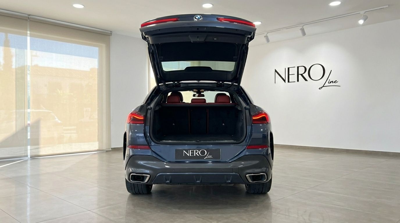 The rear view of a dark blue BMW X6 with its trunk open, showcasing the spacious cargo area and red interior seats, in Alicante.
