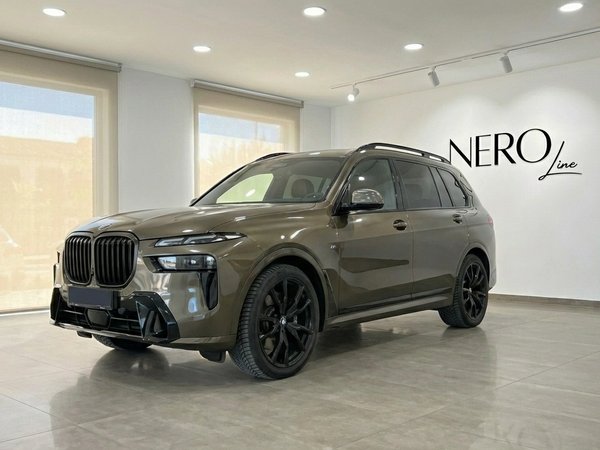 BMW X7 3.0d — Luxury SUV in Alicante The dark olive green BMW X7 3.0d luxury SUV is presented from a front three-quarter angle, parked indoors in Alicante.