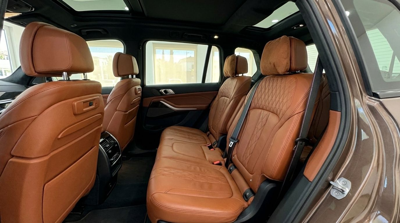 The luxurious rear interior of the 2024 BMW X7 3.0d in Alicante, featuring rich brown leather seats and a panoramic sunroof.