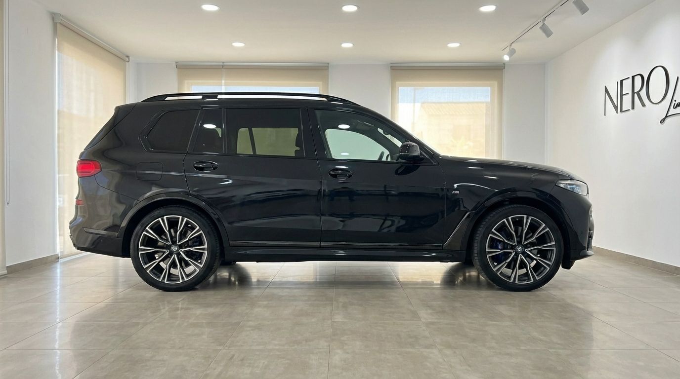 The black 2025 BMW X7 M50i Special Edition is showcased in a side profile view inside a showroom in Alicante.