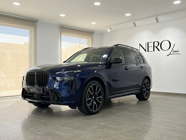 BMW X7 M60i — Vista frontal tres cuartos Madrid El BMW X7 M60i azul oscuro de 2024 se exhibe desde un ángulo frontal tres cuartos en una luminosa sala de exposiciones de Madrid.