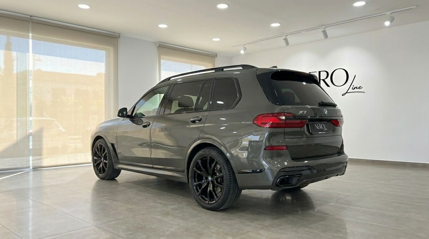 The dark grey BMW X7 luxury SUV is shown from a rear three-quarter angle, parked in a bright showroom in Alicante.